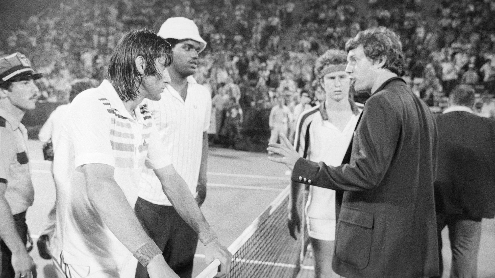 (Original Caption) John McEnroe (background) looks on as an unidentified official talks to Ilie Nastase about his show of temper and tantrum during his US Open meeting with McEnroe. The man next to Nastase is unidentified.