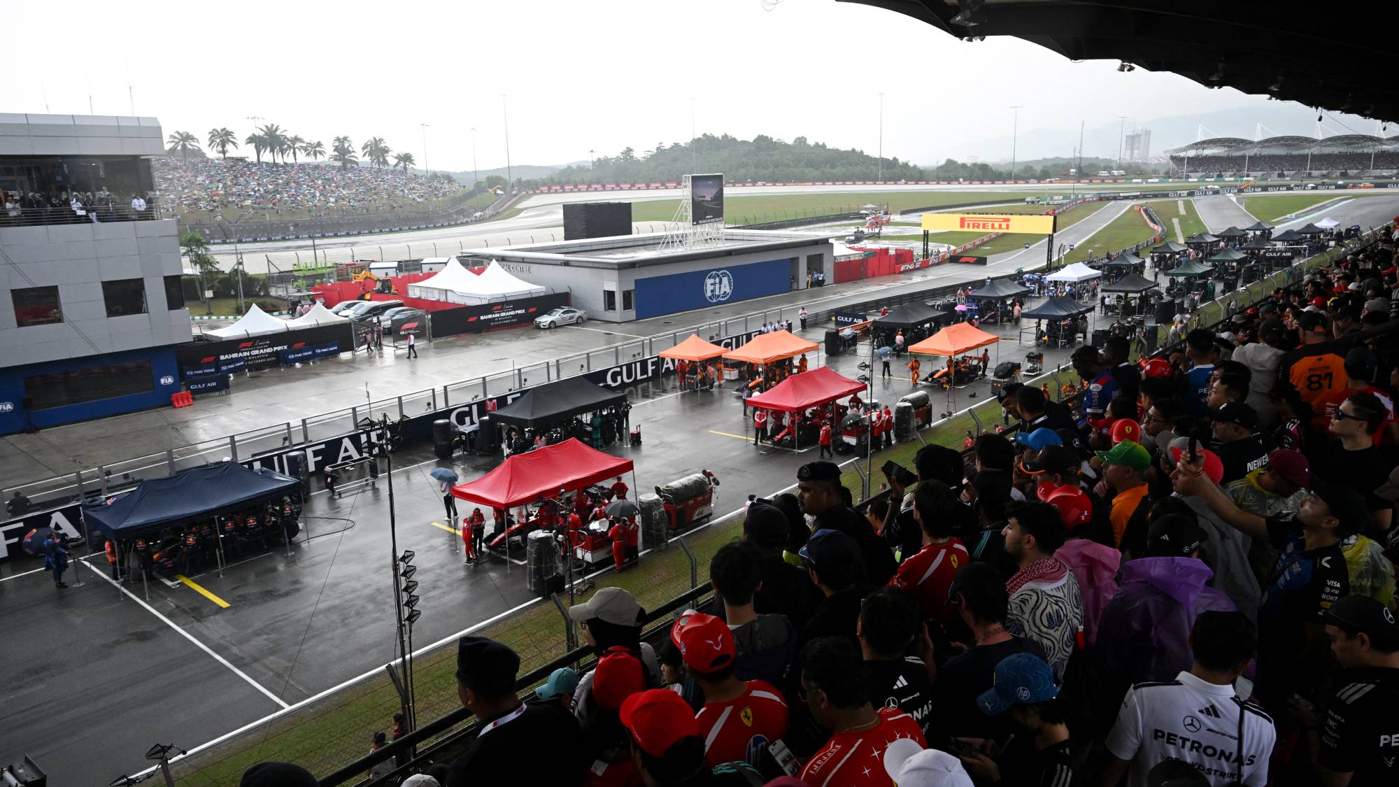 Teams gather around the cars as the start of the race has been delayed due to heave rain at the Formula One Bahrain Grand Prix in Sepang on October 4, 2026.